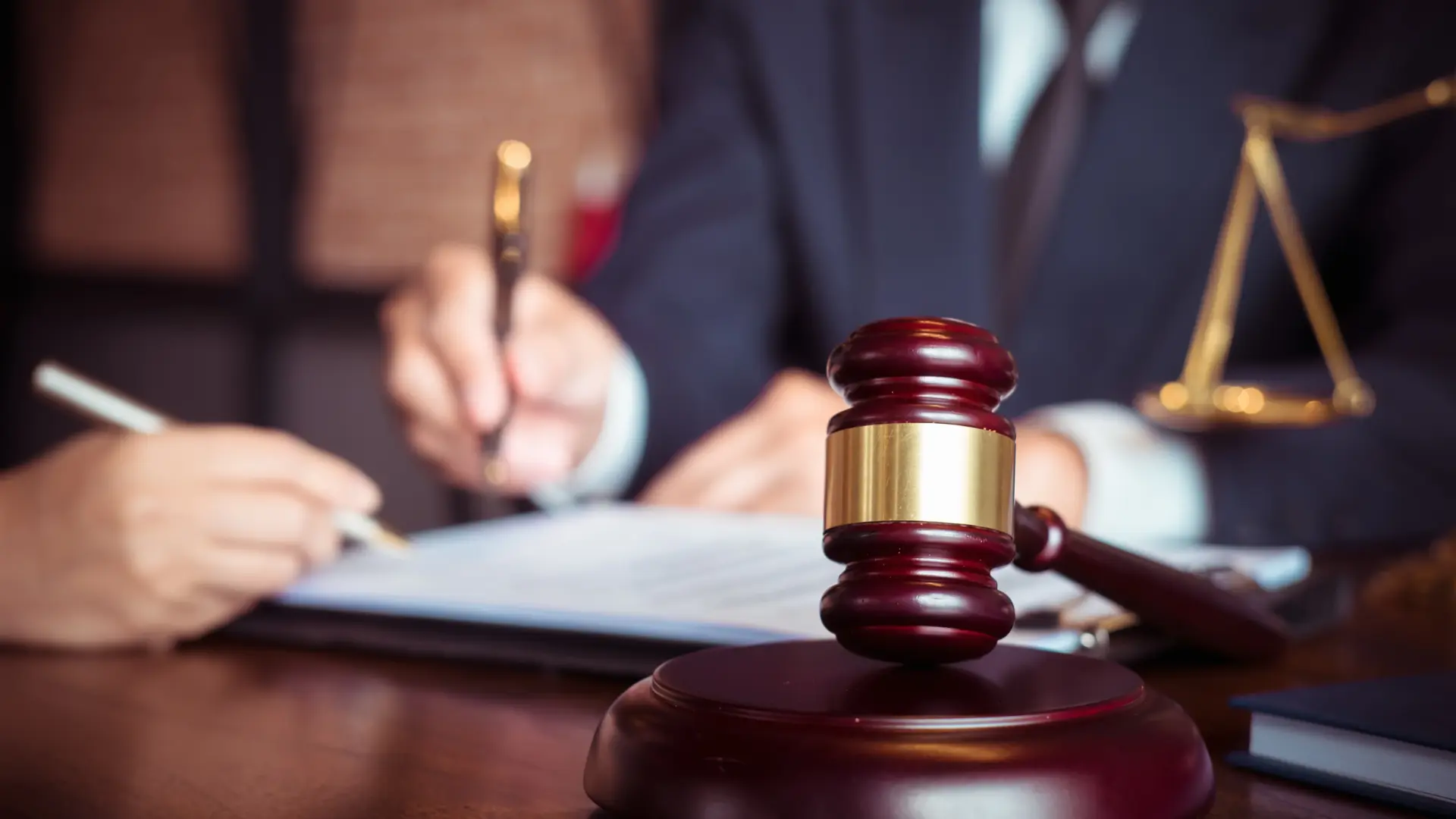 A judge's gavel with a person signing legal documents in the background.