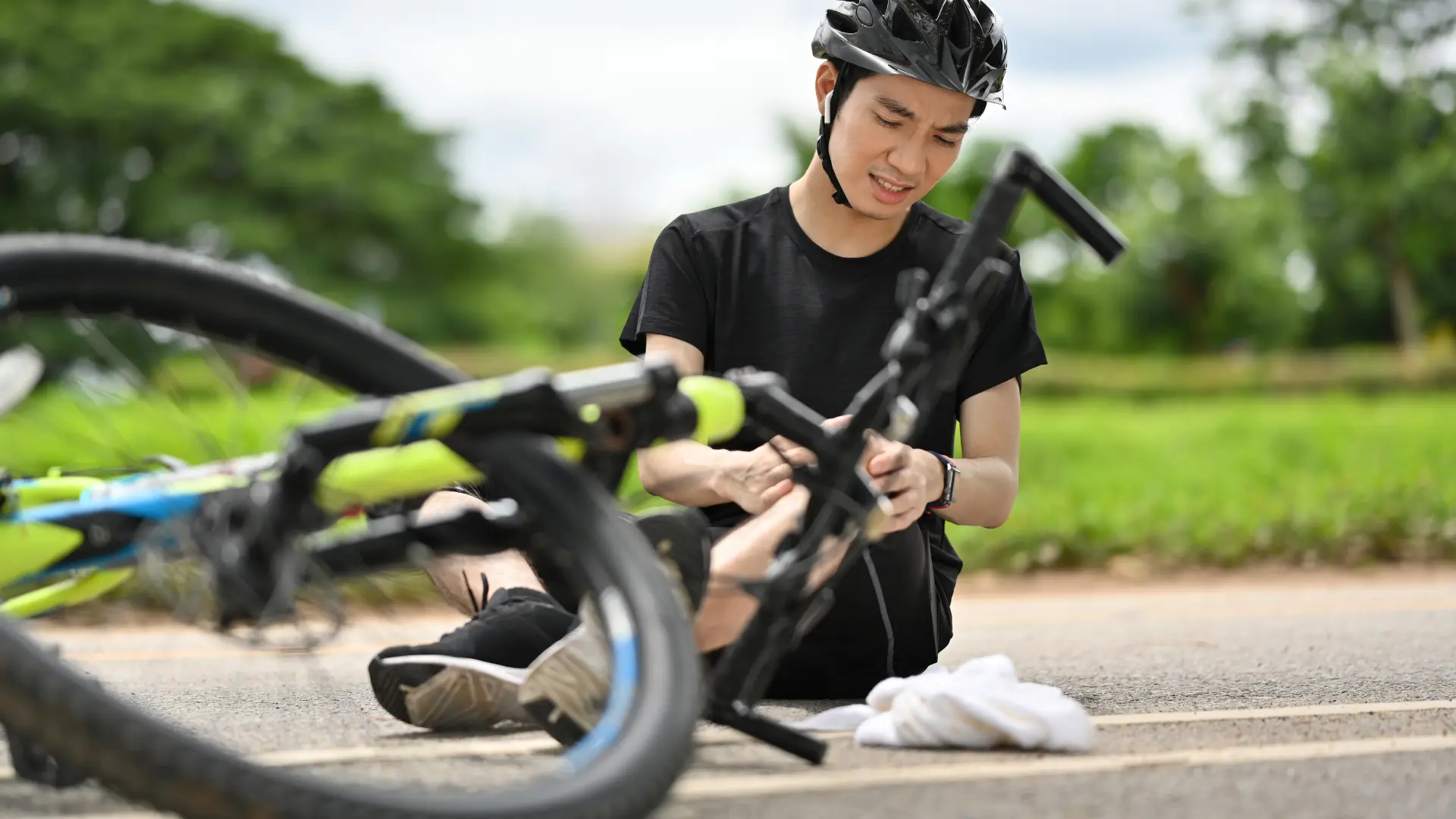 A cyclist sitting on the ground, injured after a bike accident.