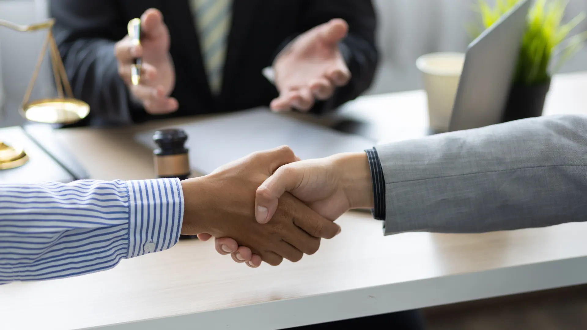 Two people shaking hands in a meeting, with a gavel in the background.