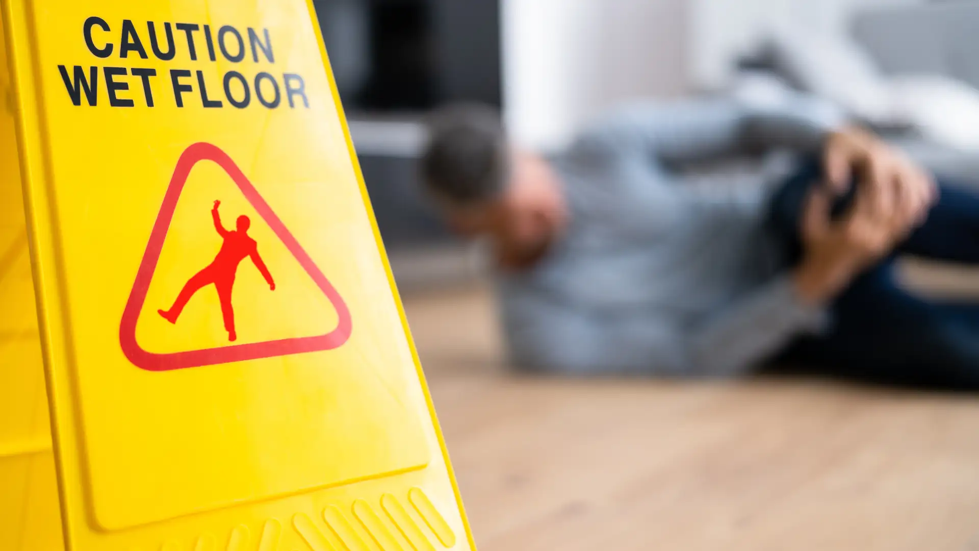 Blurred person on floor behind a 'Caution Wet Floor' sign