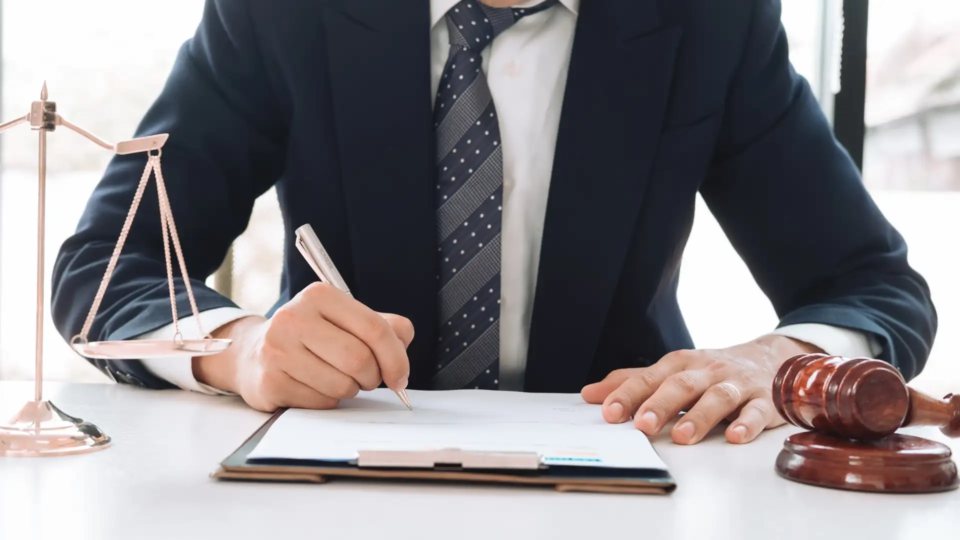 Man in a suit writing on a clipboard at a desk.