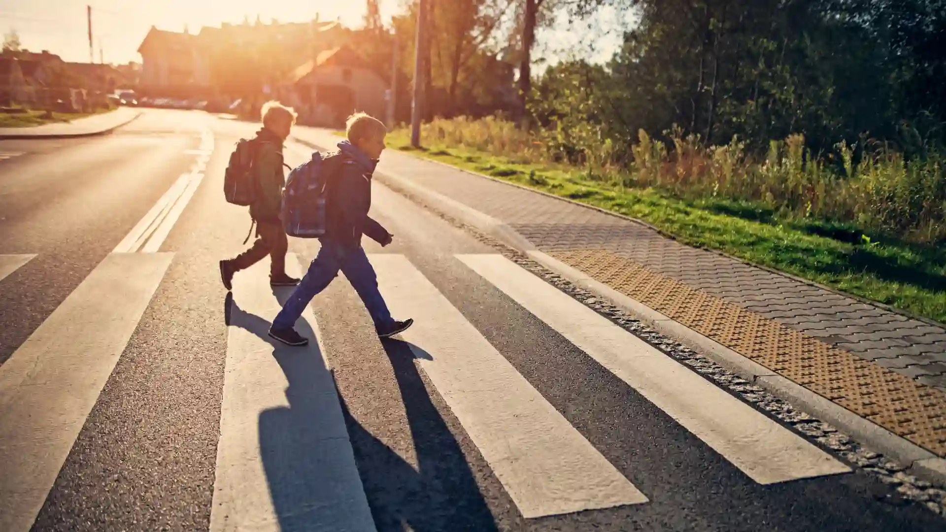 Two children with backpacks crossing a street at a crosswalk in sunlight
