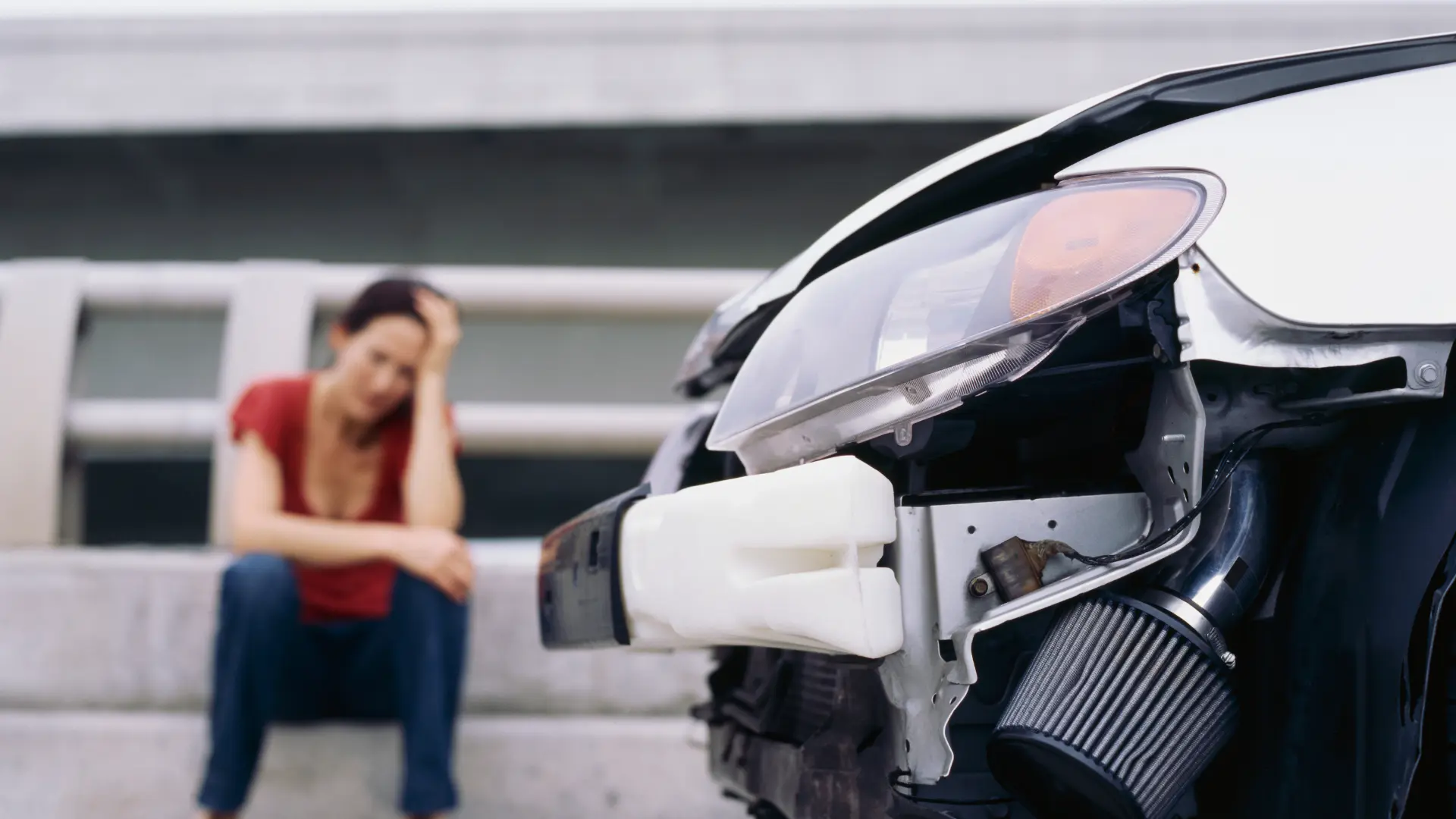 Frustrated woman sitting near a damaged car after an accident.