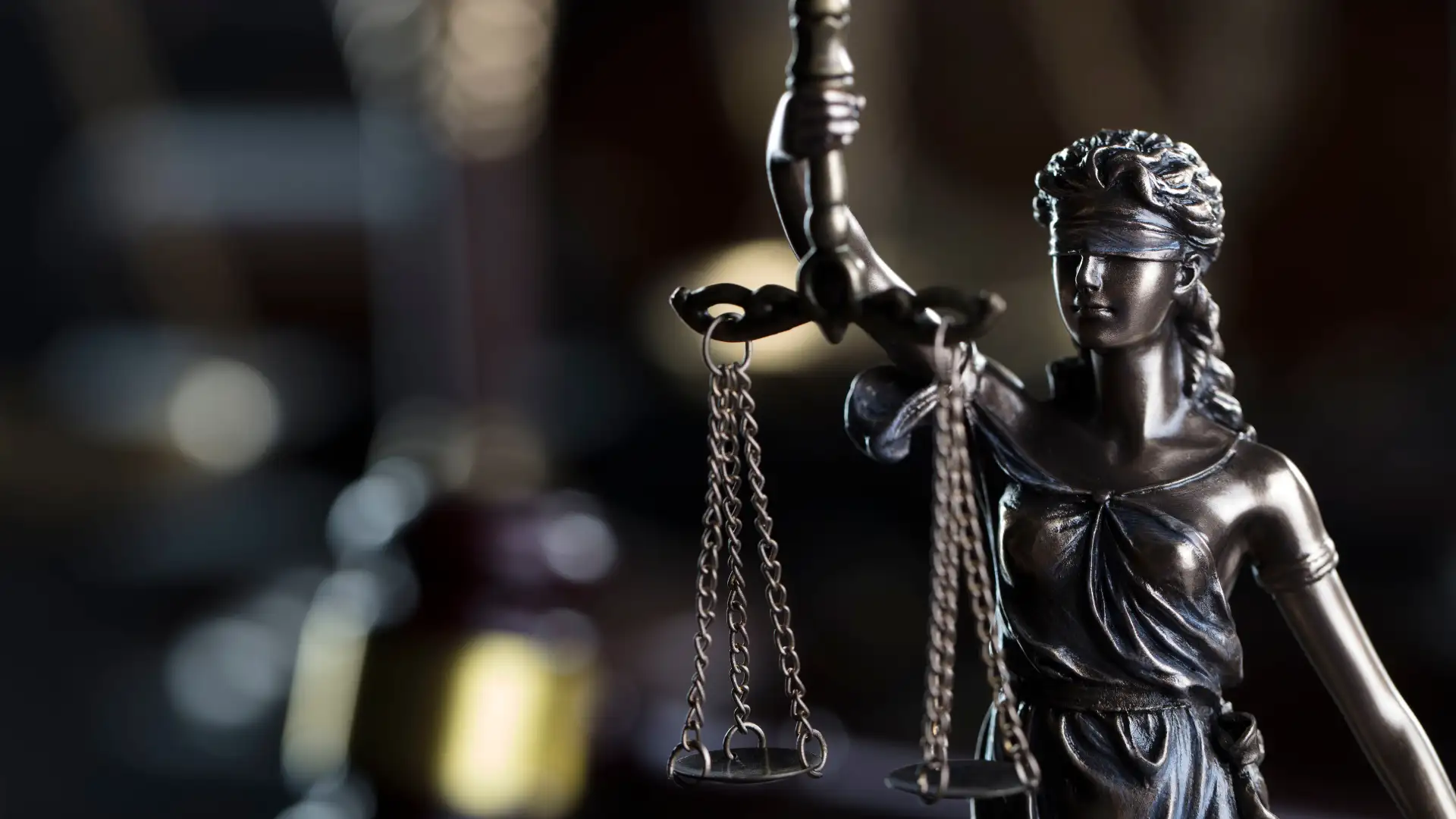Close-up of Lady Justice statue with balanced scales in a courtroom setting.