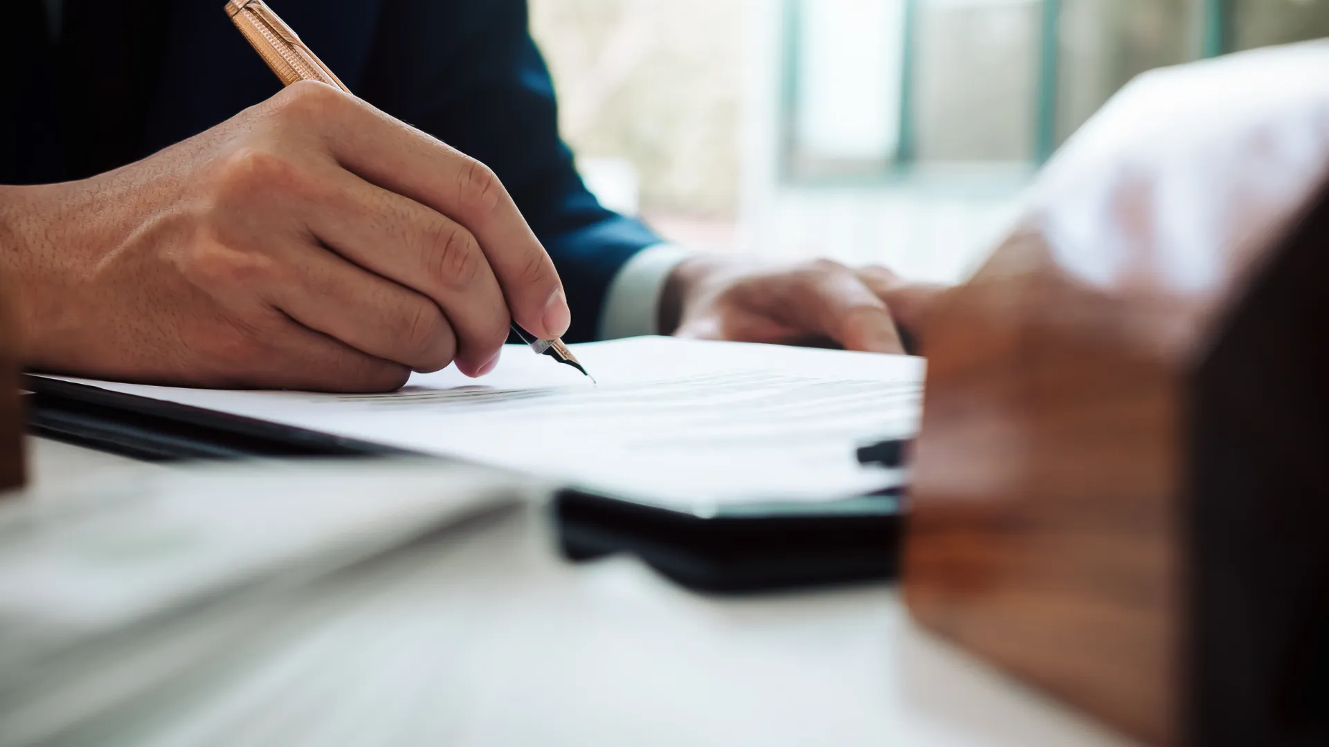Close-up of hands signing documents with a pen on a desk.